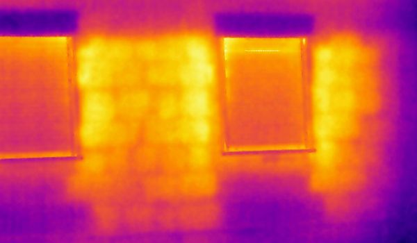 Thermografie Bild einer Mauer mit zwei Fenstern auf der man den Temperaturunterschied durch unterschiedliche Mauerwerksmaterialien erkennen kann.